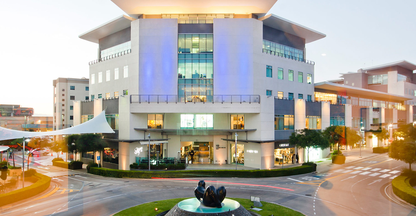 Picture of a large modern building representing the medical complex in San Jose, Costa Rica..  The building is light blue in color and has a traffic circle in front of it.