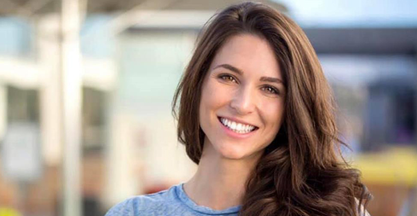 Picture of a beautiful female patient, happy with the All-on-Four dental procedure she had at Frontline Dental CR in San Jose, Costa Rica.  The picture shows a woman with long brown hair, wearing a blue blouse, and smiling while looking directly at the camera.